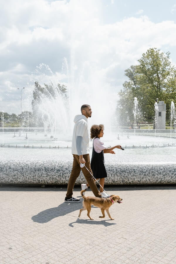 parent and child walking their dog by a fountain